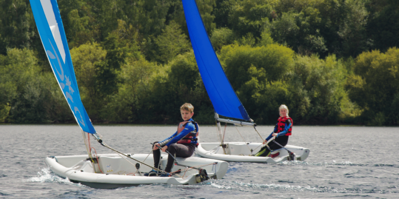 Two young sailors in dinghies on a bright day